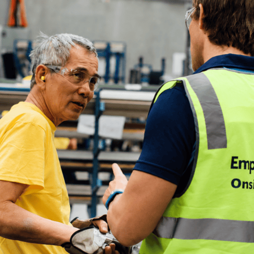 Onsite physiotherapist speaking with an industrial worker in a warehouse during a workplace assessment.