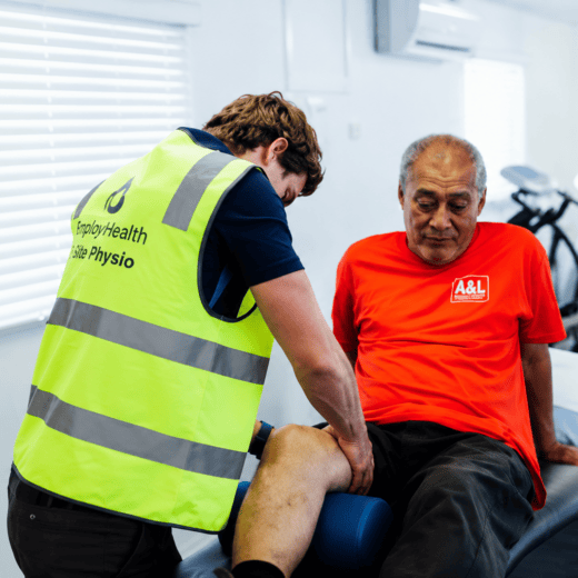 Physiotherapist assessing a worker’s leg during workplace rehabilitation.
